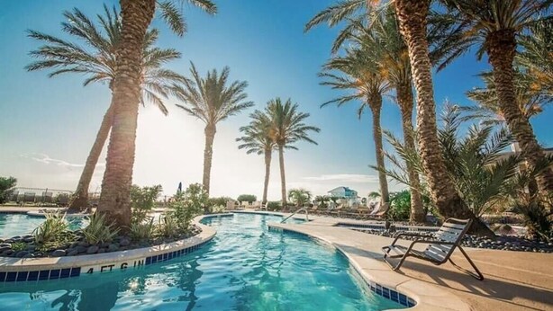 A swimming pool surrounded by palm trees and lounge chairs. - Seas The Day-Front Row-Beach Front-Next to Beach Club-3BD/2BA. Sleeps 8 (Galveston)