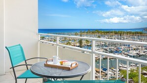 A balcony with a table, chair, and a tray with a mug, a croissant, and a fruit. - Ocean-Marina Sunset Views Condo with Full Kitchen at Ilikai Hotel by Beach (Honolulu)