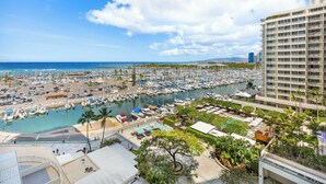 A marina with numerous boats docked, a large building with balconies, and a clear blue sky. - Ocean-Marina Sunset Views Condo with Full Kitchen at Ilikai Hotel by Beach (Honolulu)