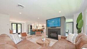 A modern living room with a large brown leather sofa, a coffee table, and a fireplace. There is a kitchen in the background with a dining area. - Bayside Oasis with Hot Tub & Game Room (Dennis)