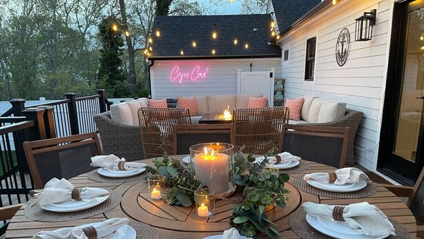 An outdoor dining area with round tables set for four, surrounded by wicker chairs. A large candle centerpiece and small candles on each table create a warm ambiance. - Bayside Oasis with Hot Tub & Game Room (Dennis)