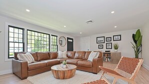 A spacious living room with a brown leather sectional sofa, a round wooden coffee table, and a woven chair. - Bayside Oasis with Hot Tub & Game Room (Dennis)