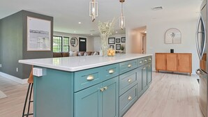 A modern kitchen with teal cabinetry, a white countertop, pendant lighting, and a wooden cabinet. - Bayside Oasis with Hot Tub & Game Room (Dennis)