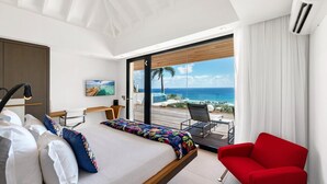 Een moderne hotelkamer met een bed, een rode fauteuil, een bureau en uitzicht op de oceaan.