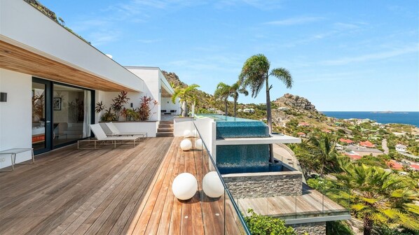 Una casa moderna con terraza de madera, piscina y vista al océano.