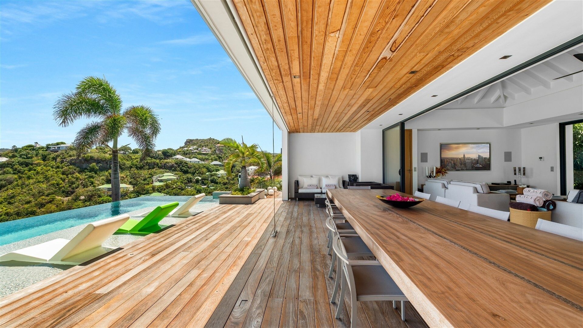 Un espace de vie extérieur moderne, doté d’une terrasse en bois, d’une piscine et offrant une vue sur un paysage luxuriant.