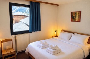 A hotel room with a bed, a chair, a window with curtains, a radiator, and a wall-mounted light. - Nice flat with balcony view Mont Blanc | Parking (Chamonix-Mont-Blanc)