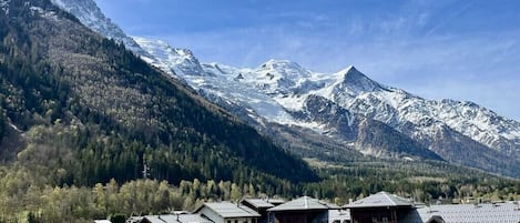 Un complejo turístico de montaña con edificios de estilo chalete, una pista de esquí y picos nevados al fondo.