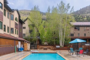 A swimming pool with a deck area, surrounded by buildings and trees.