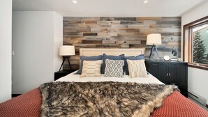 A bedroom with a wooden wall panel, a bed with multiple pillows, two bedside lamps, a nightstand, and a window with a view of a tree. - Lulu 6J Walk to Lift 7 + Pool & HotTub - 2 Bedroom+Loft, 3 Bathroom, Sleeps 6 (Telluride)