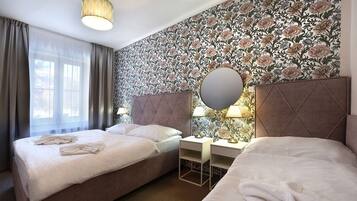 Una camera d'albergo con due letti, un grande specchio e carta da parati con motivi floreali.