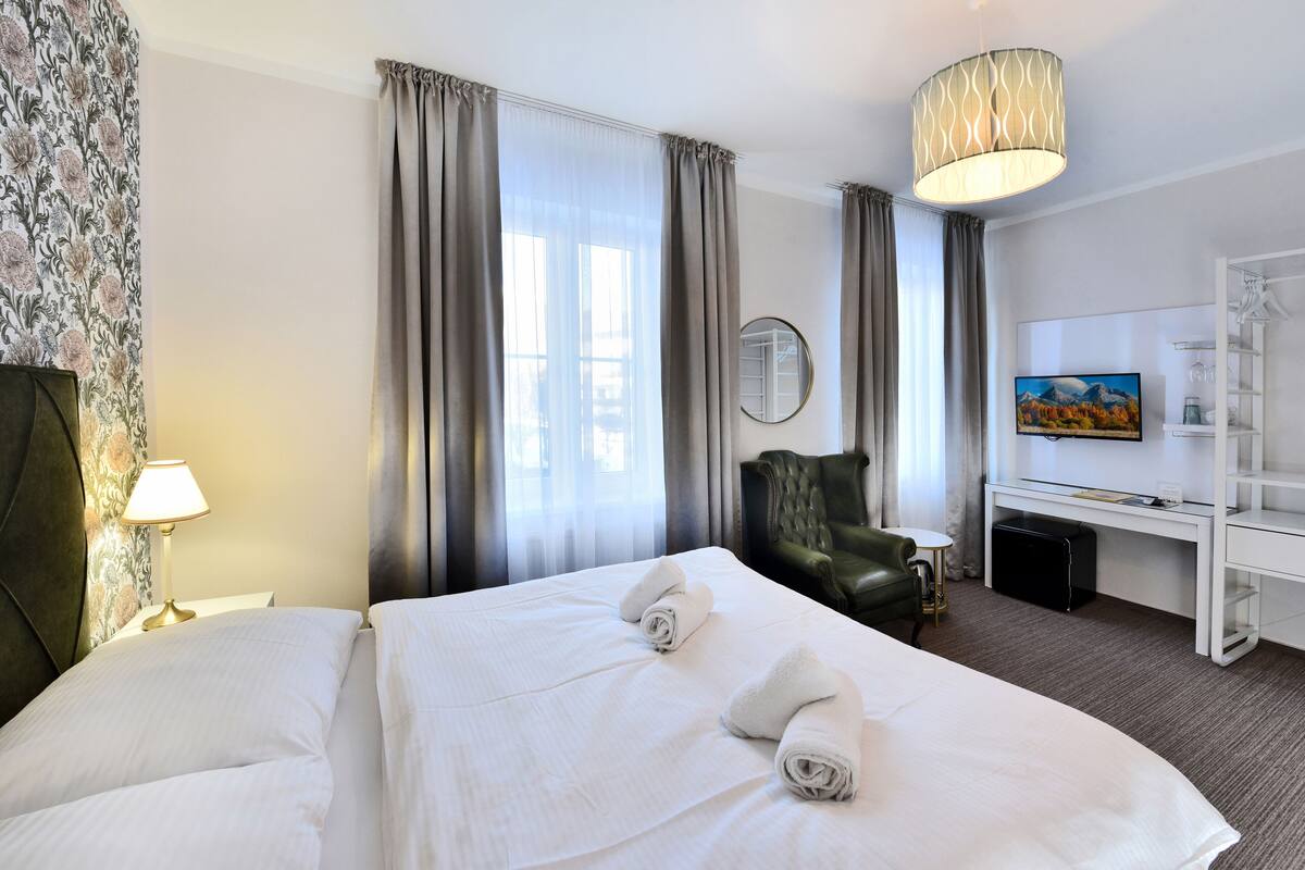 A hotel room with a large bed, a desk, a chair, a TV, and a lamp.