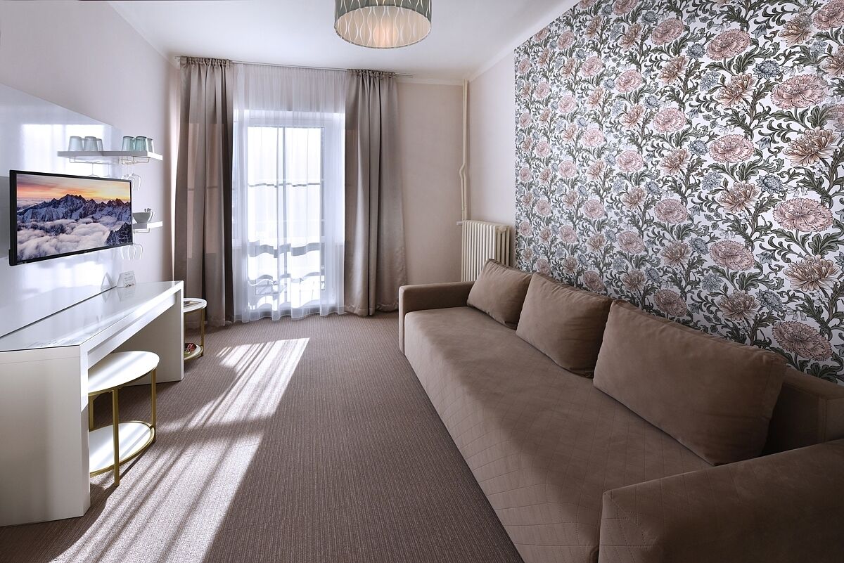 Een moderne hotelkamer met een beige bank, een flatscreen televisie, een bureau en een groot raam met gordijnen.
