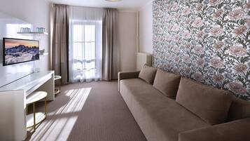 Een moderne hotelkamer met een beige bank, een flatscreen televisie, een bureau en een groot raam met gordijnen.