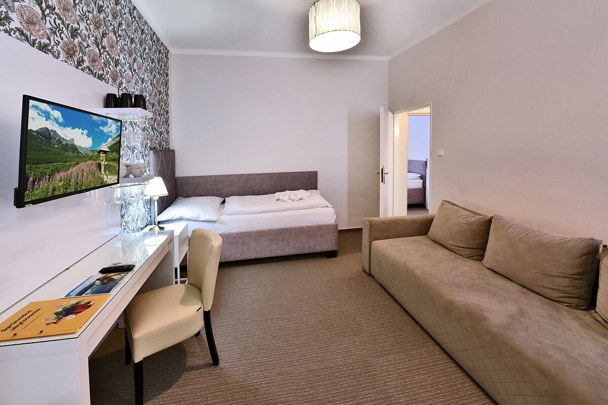 Hotellihuone, jossa on sänky, työpöytä tuolilla, sohva, televisio ja lamppu.
