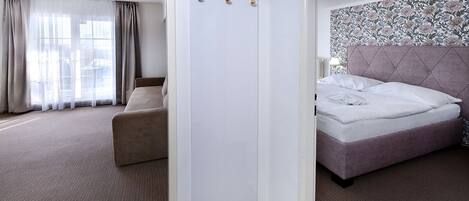 Una habitación de hotel con cama, sofá, armario y un amplio ventanal con cortinas.