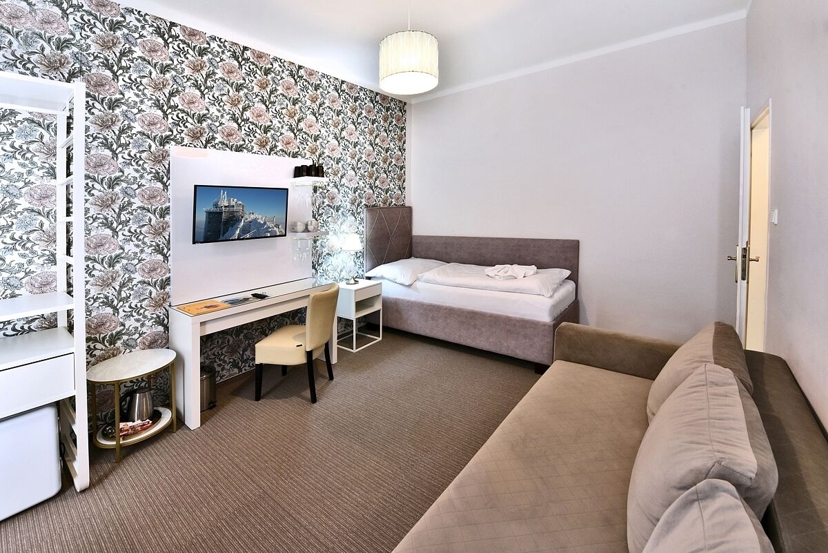 A hotel room with a bed, a desk with a chair, a TV mounted on the wall, and a sofa.