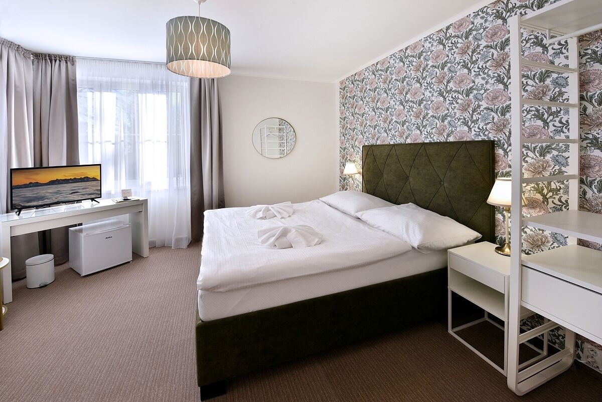 Een hotelkamer met een bed, bureau, televisie en raam met gordijnen.