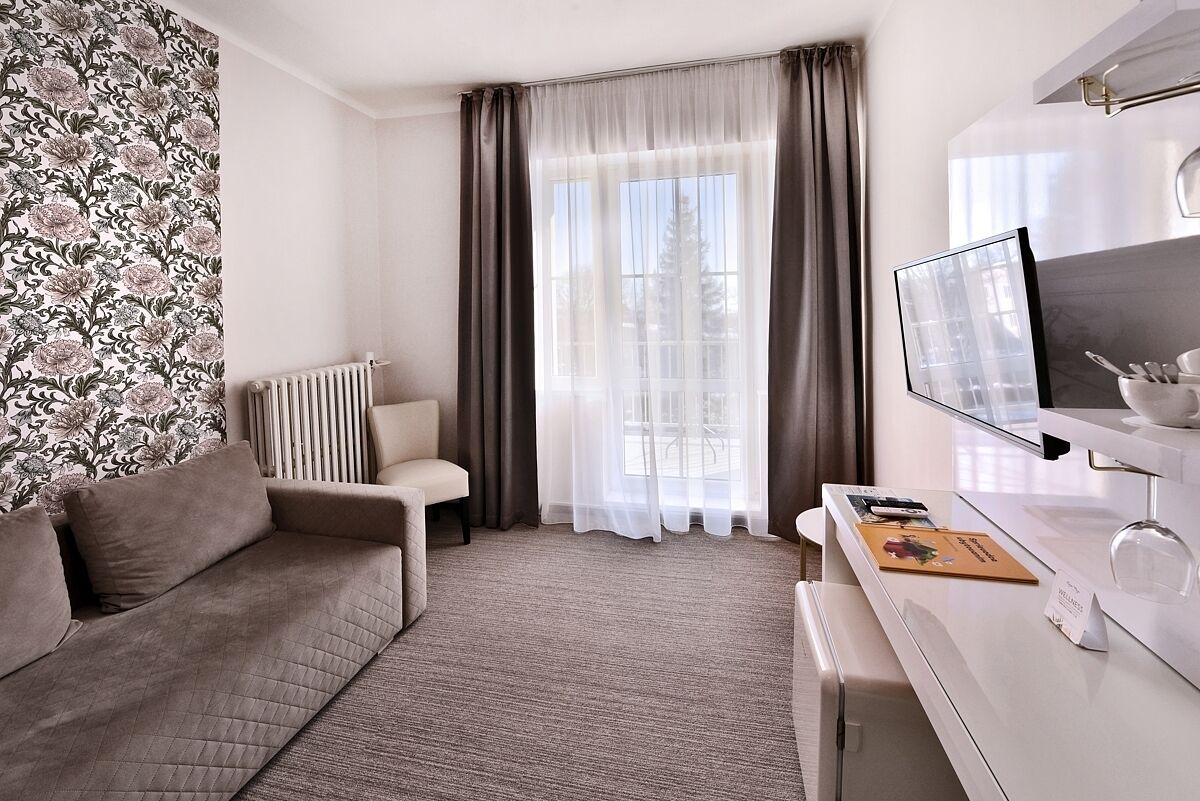Una habitación de hotel moderna con sofá, escritorio con computadora, radiador y cortinas traslúcidas.