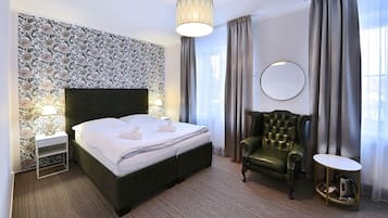 Et hotelværelse med en stor seng, en grøn lænestol, et rundt spejl og et lille bord med elkedel.