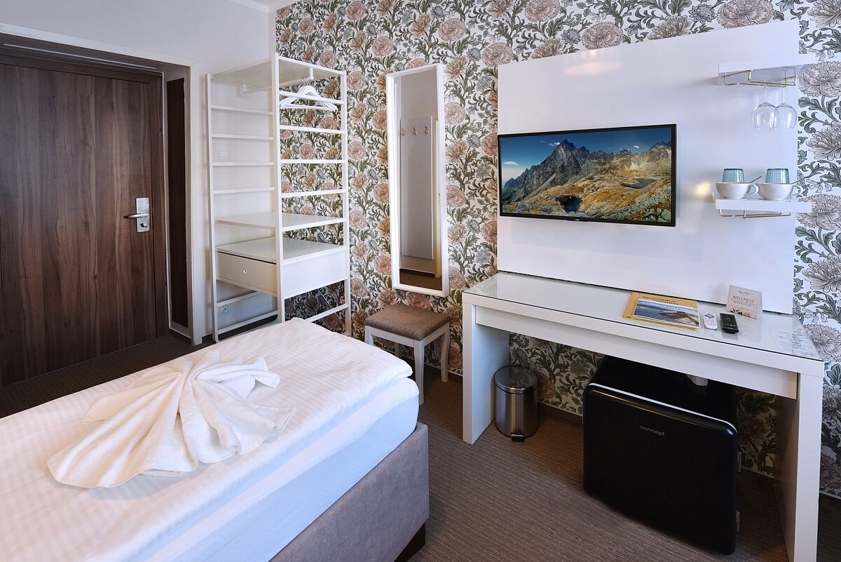 A hotel room with a bed, a desk with a computer, a TV, and a wardrobe.