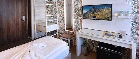 A hotel room with a bed, a desk with a computer, a TV, and a wardrobe.