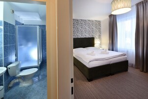 Habitación de hotel con ducha, inodoro y cama con cabecera.