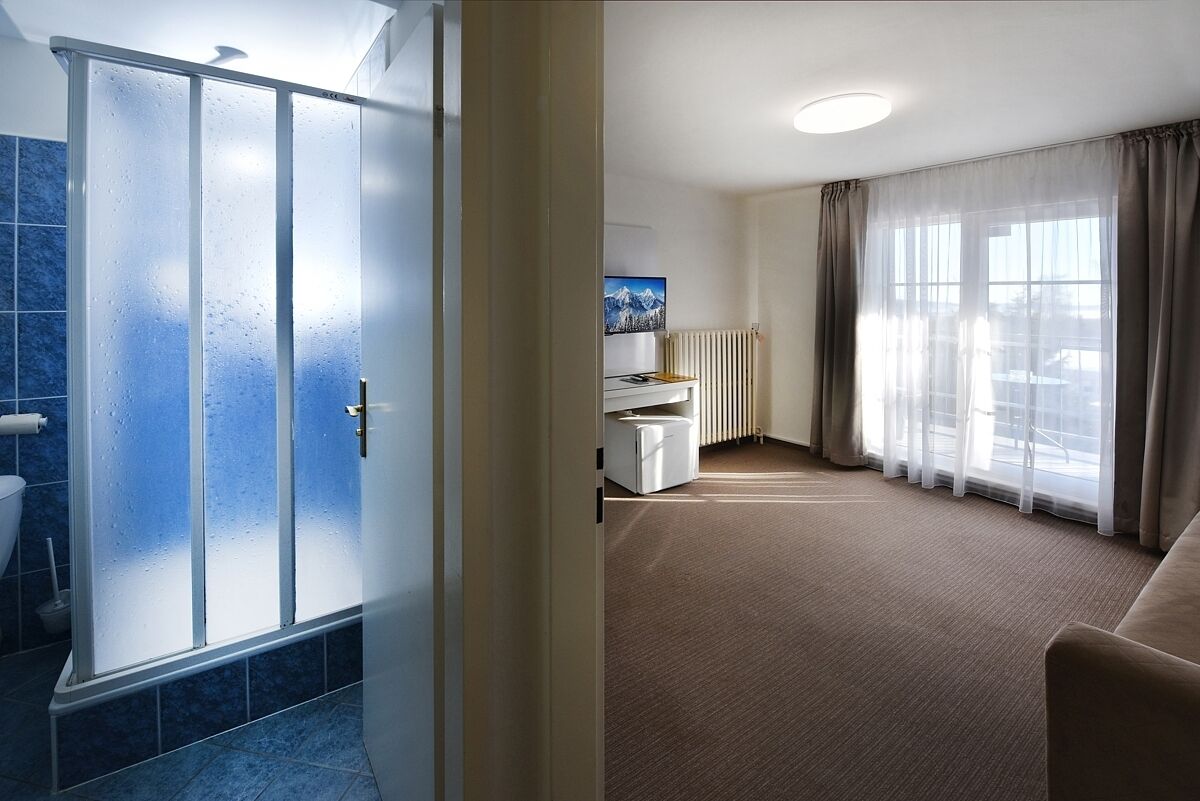 Habitación de hotel con ducha, radiador, sofá y un amplio ventanal con cortinas.