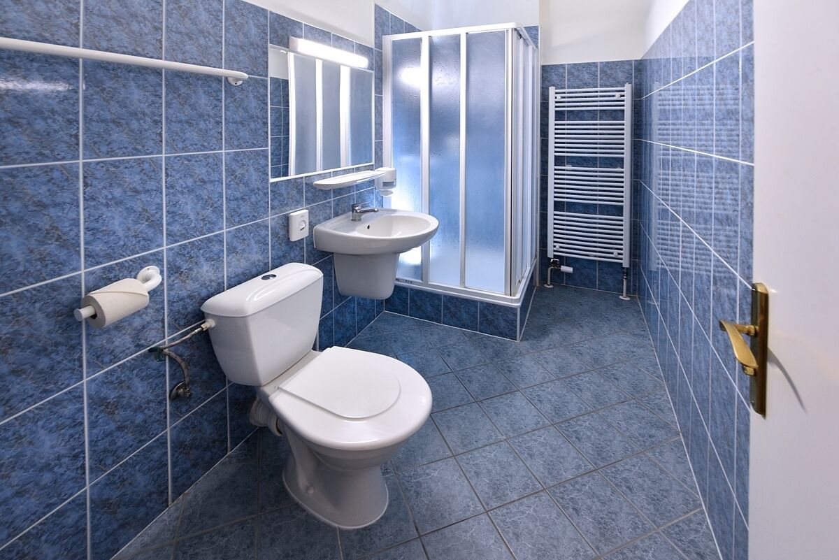 A bathroom with blue tiles, a toilet, a sink, a shower, and a towel rack.