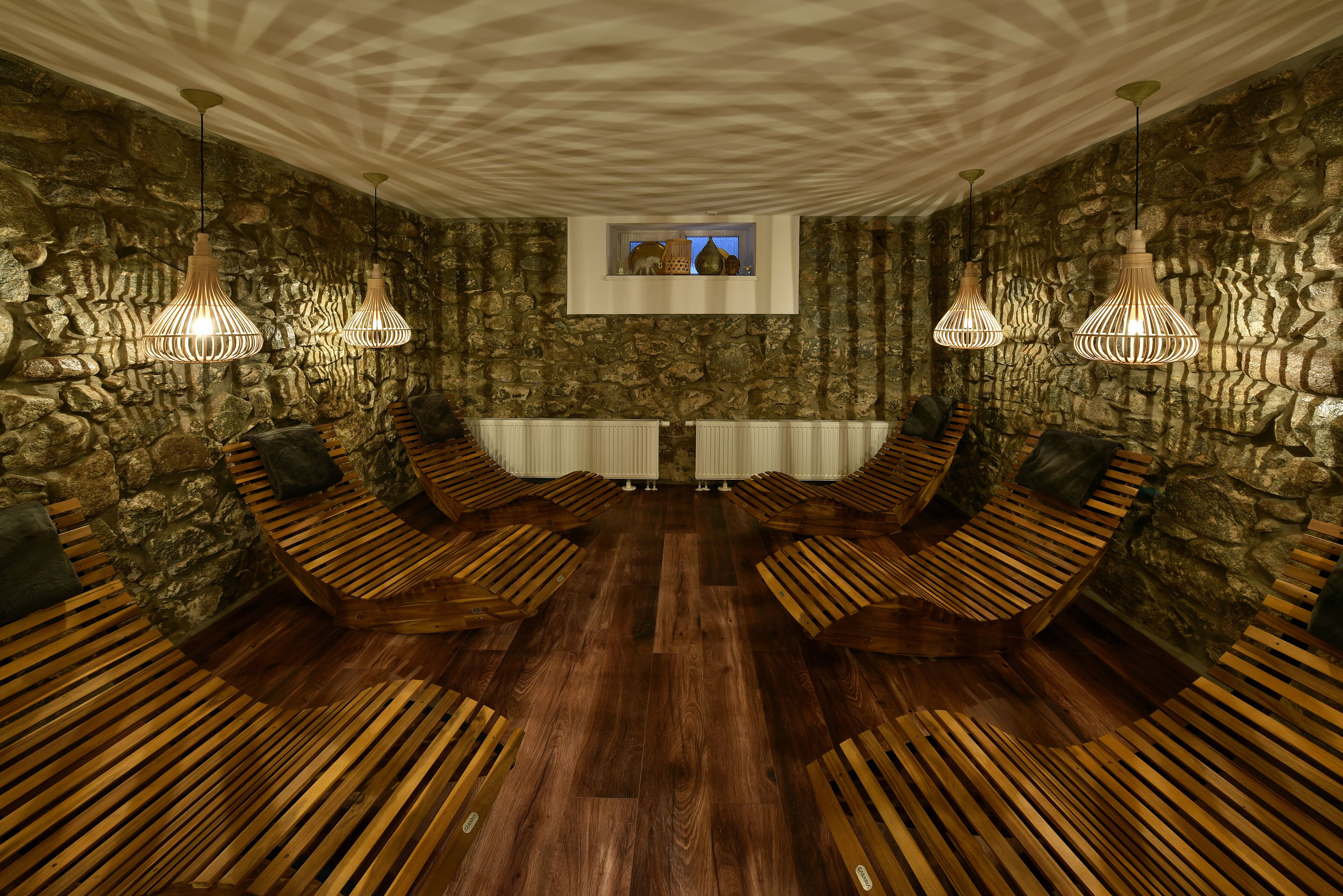 Una habitación con pared de piedra, bancos de madera y lámparas colgantes.