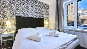 A hotel room with a large bed, floral wallpaper, two bedside lamps, and a window with a snowy mountain view.