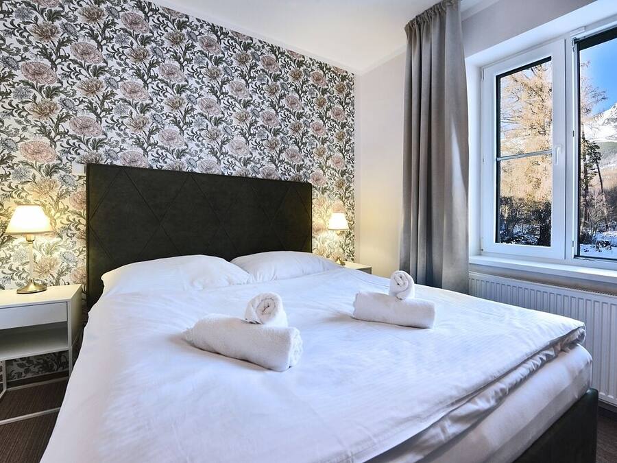 A hotel room with a large bed, floral wallpaper, two bedside lamps, and a window with a snowy mountain view.
