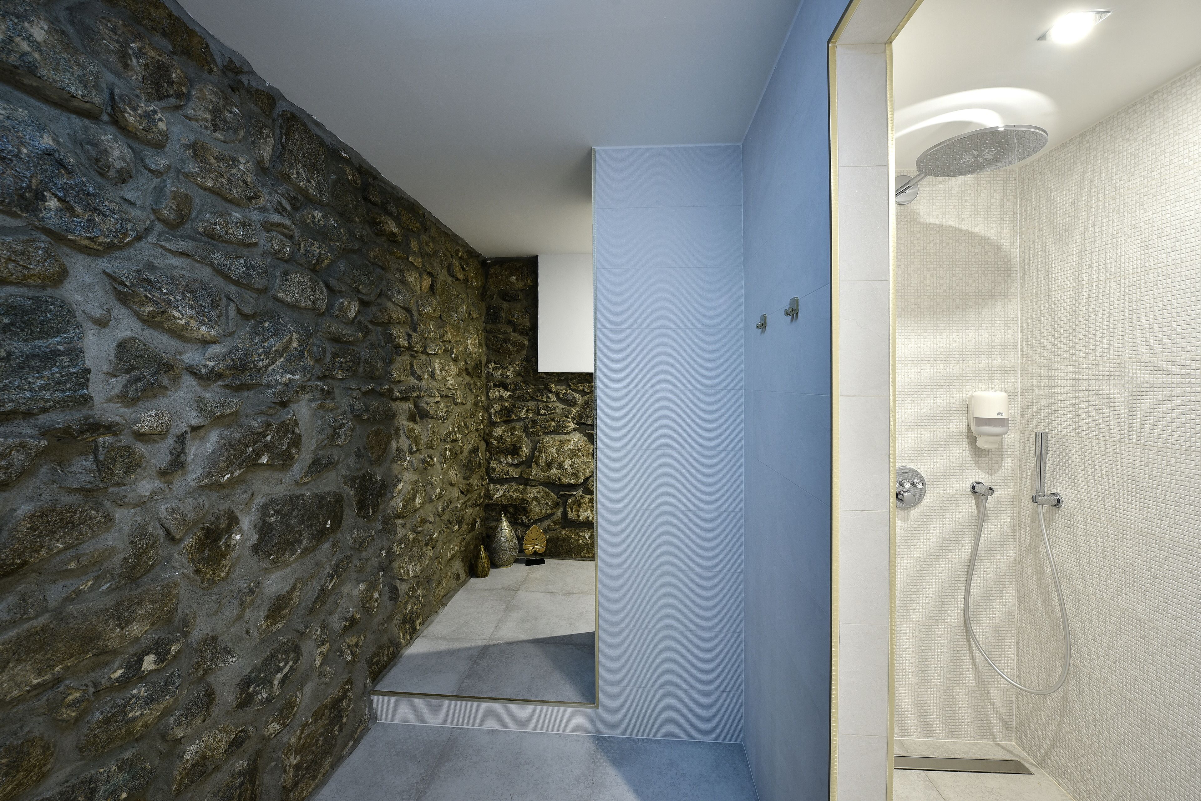 A modern bathroom with a stone wall, a shower area, and a tiled floor.