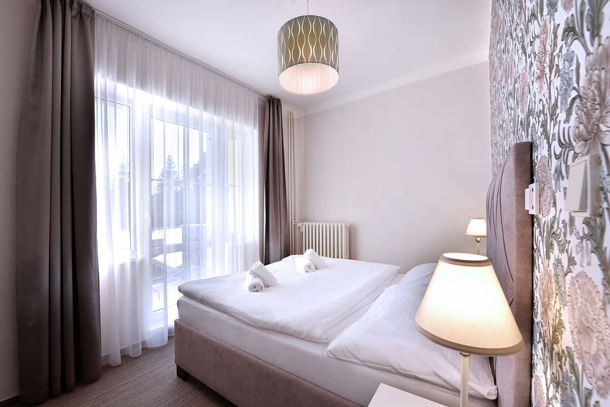 A hotel room with a large bed, a bedside lamp, a radiator, and a window with curtains.