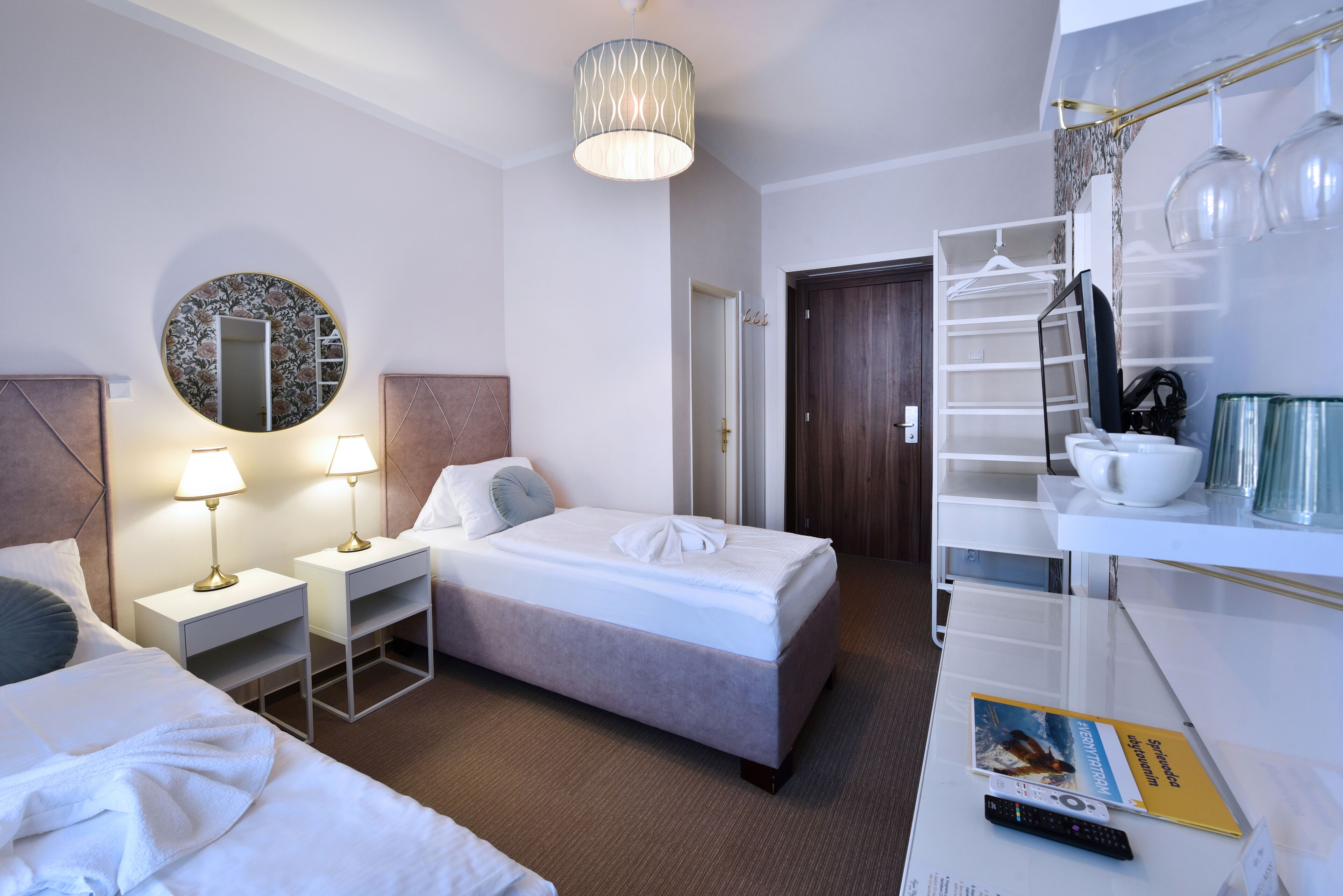 A hotel room with a bed, two bedside tables with lamps, a mirror, a wardrobe, and a shelf with a remote control.