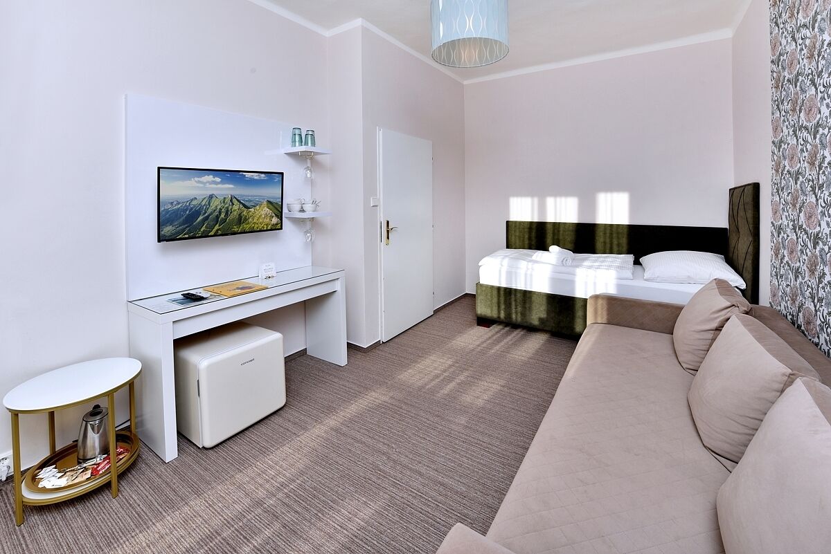 Ein Hotelzimmer mit einem Bett, einem Schreibtisch, einem Sessel, einem kleinen Tisch, einem Fernseher und einem Fenster.