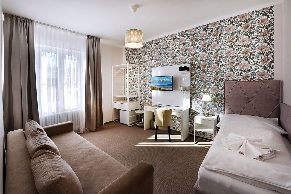 A hotel room with a bed, a desk, a chair, a wardrobe, and a large window with curtains.