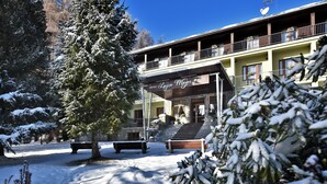 Een hotel met een overdekte ingang, buiten zitplaatsen en een besneeuwde omgeving.
