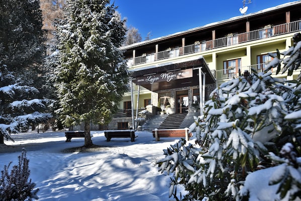Un hotel con entrada cubierta, mesas al aire libre y paisajes nevados.
