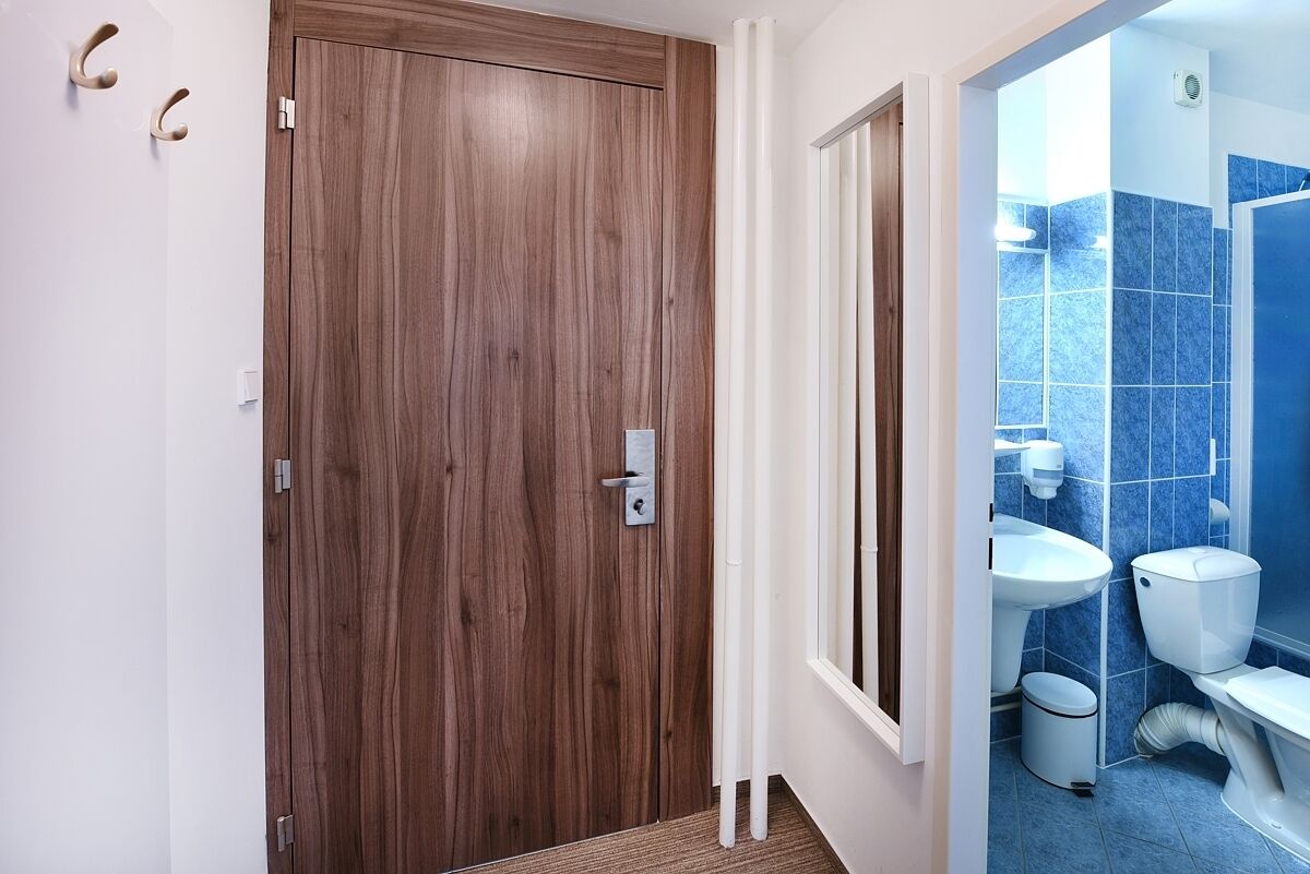 Une porte en bois avec une poignée, un mur blanc et une salle de bain avec un mur recouvert de carreaux bleus et des accessoires blancs.