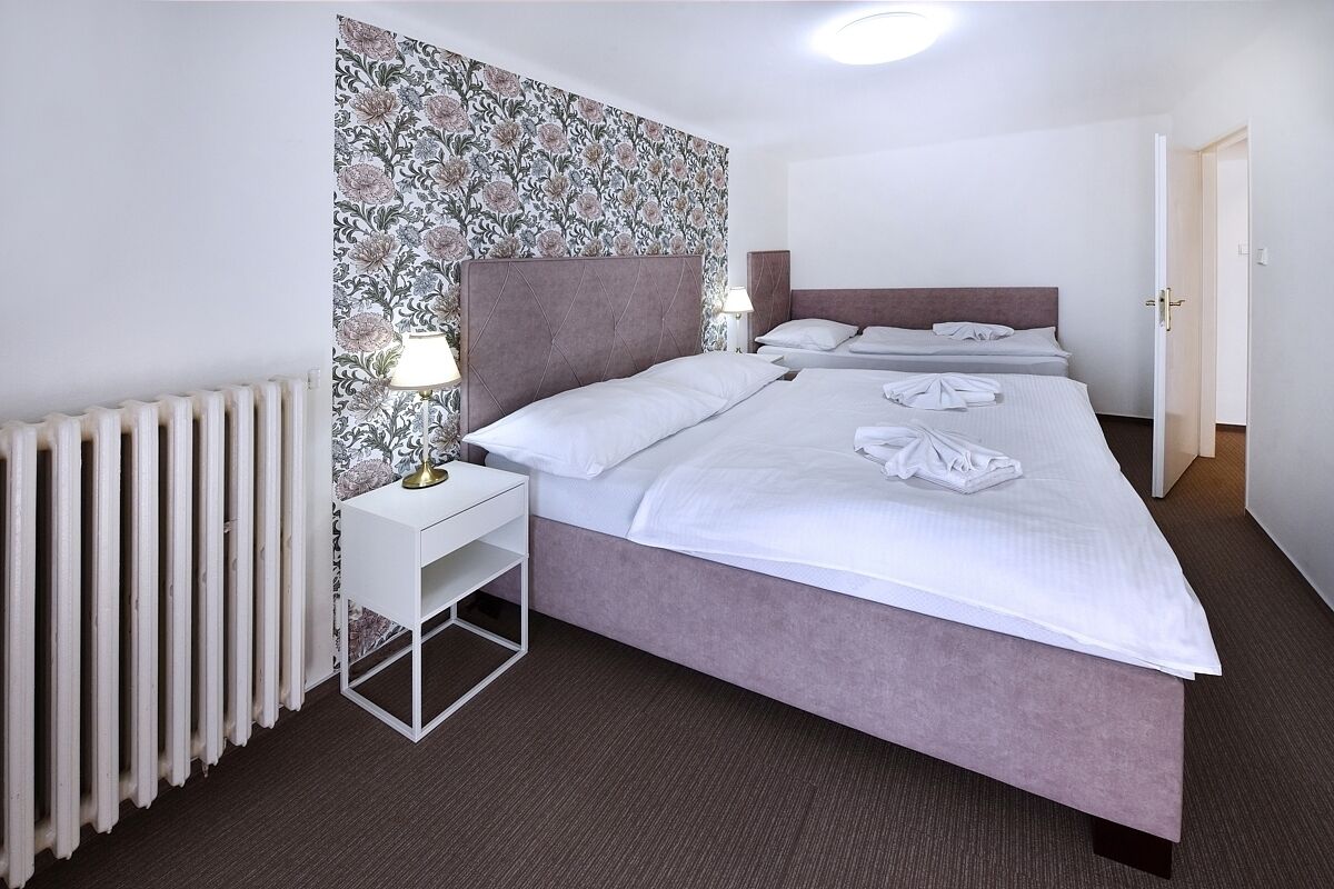 Camera d'albergo con un letto grande, un comodino con una lampada, un termosifone e una parete decorata con un motivo floreale.