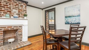 A dining area with a brick fireplace, wooden dining table, and chairs. - Waldburg Manor | Pet Friendly, Historic Savannah! (Savannah)