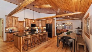 Une cuisine spacieuse dotée de meubles en bois, d’un îlot central avec des tabourets et d’un coin repas avec une table et des chaises en bois.