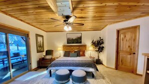 Une chambre dotée d’un grand lit, de deux tables de chevet, d’un ventilateur de plafond et offrant une vue sur l’extérieur grâce à une porte-fenêtre coulissante.