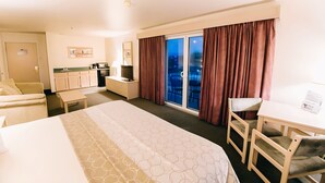 A hotel room with a bed, a desk, a chair, a small kitchenette, and a balcony with curtains. - North Shore Inn (Overton)