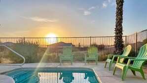 A swimming pool with a sunset in the background, surrounded by a fence and green chairs. - North Shore Inn (Overton)