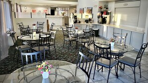 A dining area with multiple round tables and chairs, a kitchen area with appliances, and a ceiling fan. - North Shore Inn (Overton)
