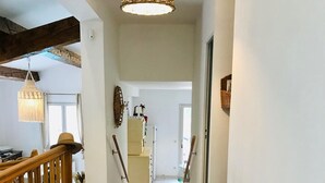 A spacious hallway with a wooden staircase, a woven ceiling light, and a view into a kitchen area. - Villa in a green setting, not overlooked, facing the village of Bargemon (bargemon)