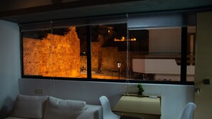 A modern living room with a large window, a sofa, two white chairs, and a desk with a plant. - Kastren Rooms (Chania)