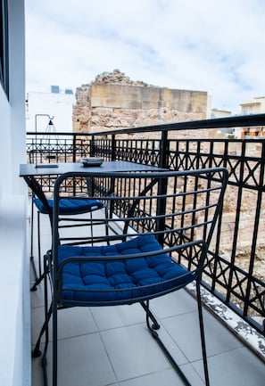 A balcony with a table and chairs, a view of a stone wall, and a tiled floor.